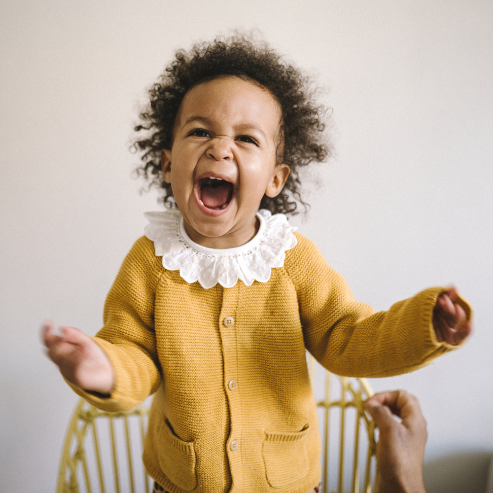 En jätteglad liten tjej i gul tröja och med vit krage i närbild. 