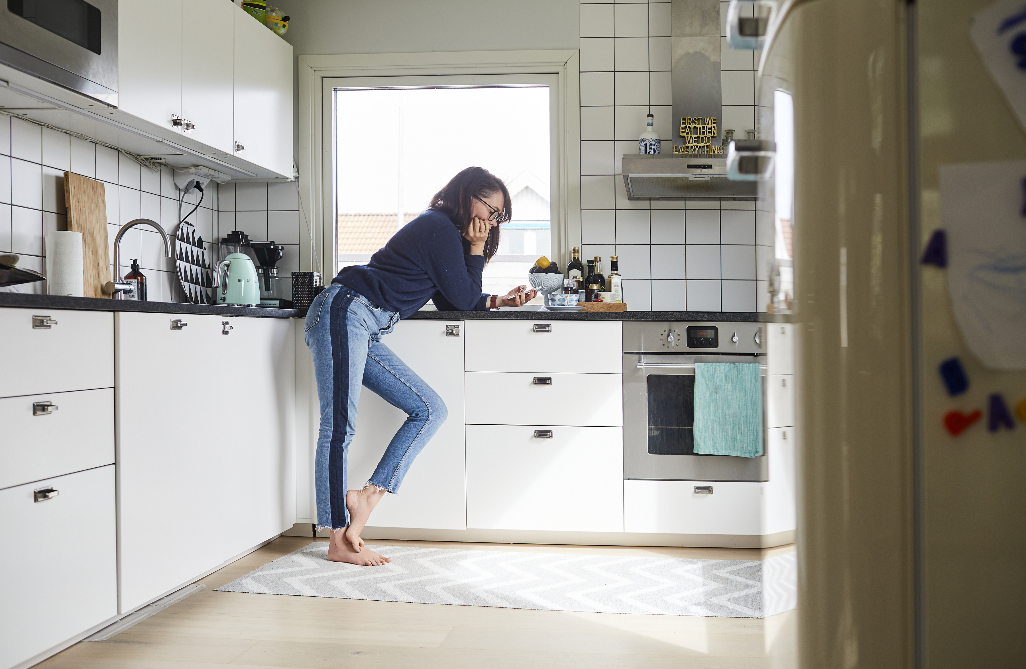 Ung kvinna hänger på en köksbänk och tittar i sin telefon. 