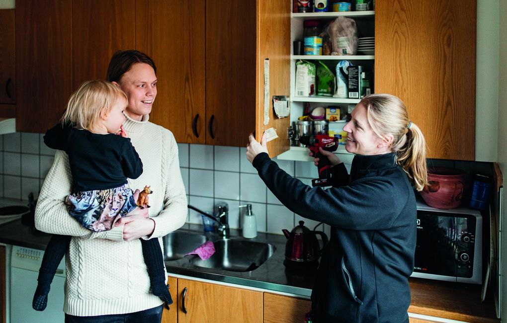 En ung pappa med sin dotter på armen i ett kök där en kvinna från Mölndalsbostäder fixar ett köksskåp. 