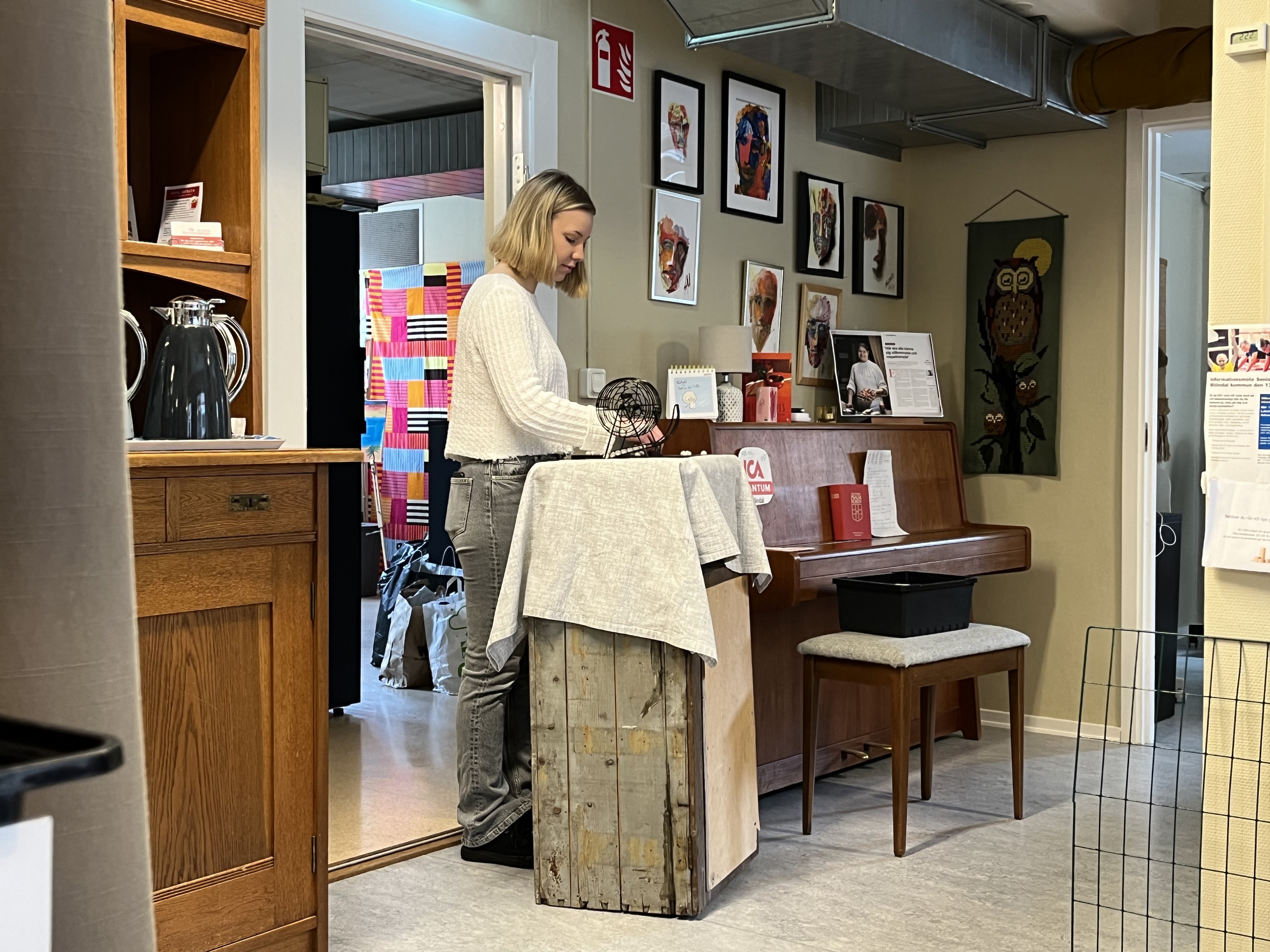 Ung kvinna står i en liten lokal med en bingosnurra och leder ett bingo för organisationen Hela människan. 