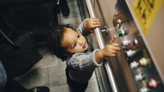 Litet barn sträcker sig efter våningsknapparna i en hiss.